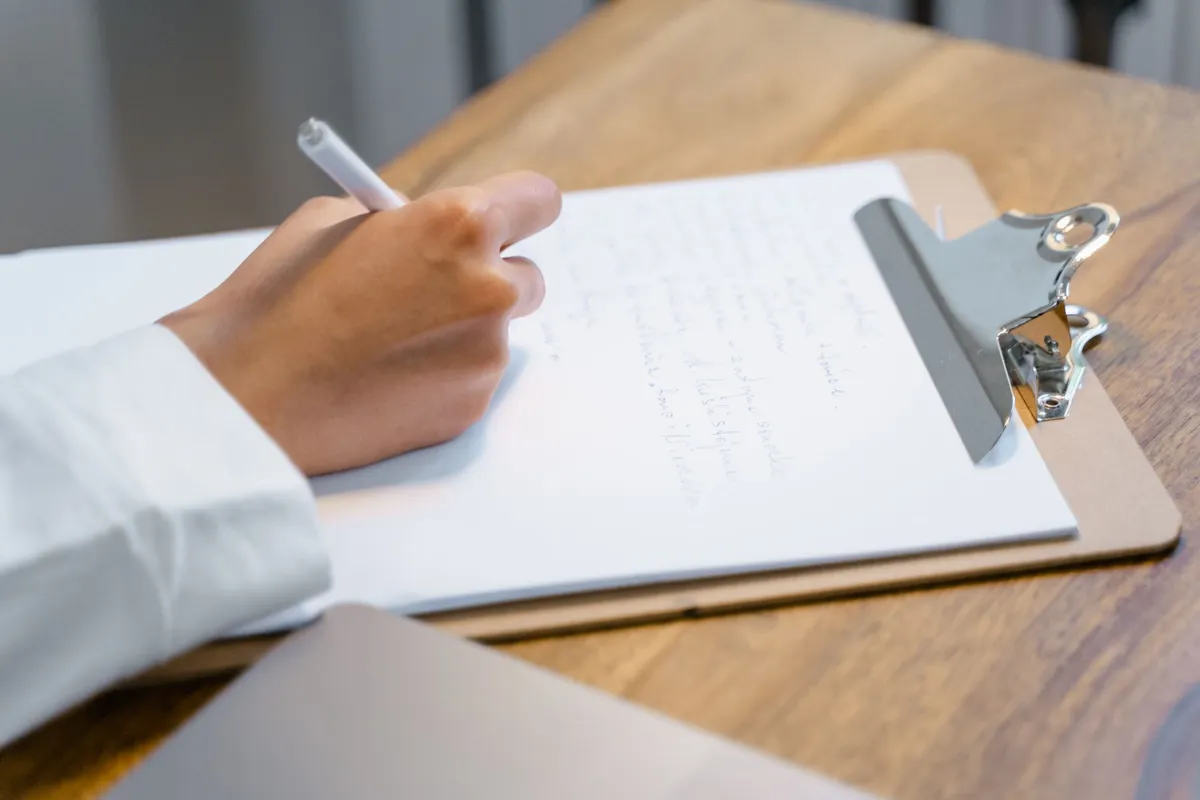 Hand mit Stift notiert den Umfang eines Umzugs auf einem Klemmbrett am Holztisch