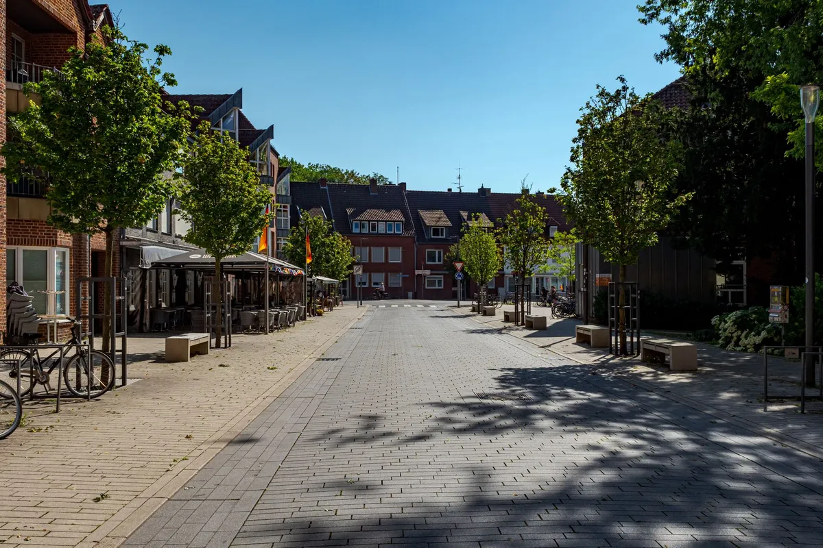Sonnige gepflasterte Fußgängerzone mit Bäumen, Backsteinhäusern und Außengastronomie