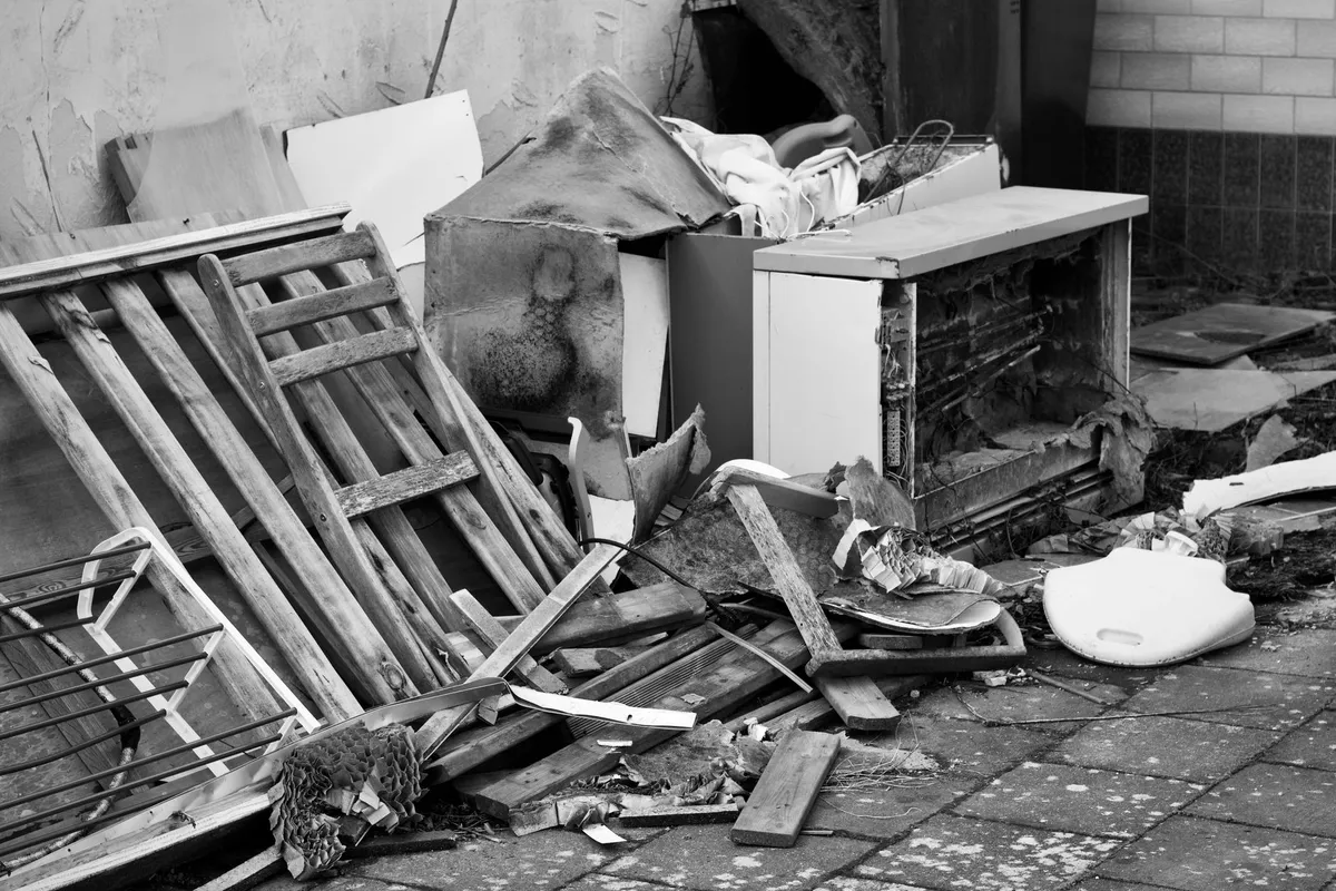 Haufen aus Sperrmüll mit Holzlatten und altem Schrank vor einer Hauswand, Schwarzweissfoto