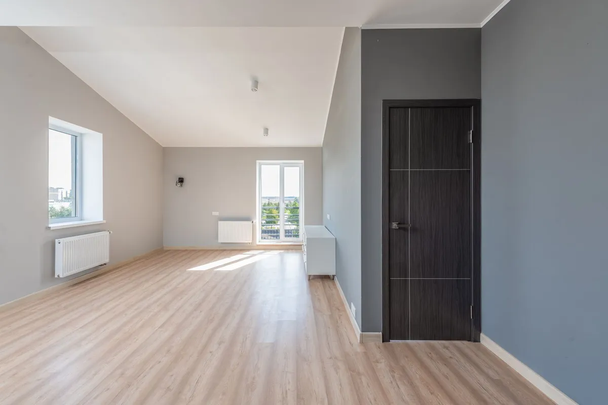 Leer geräumtes Zimmer mit Laminatboden, Heizkörper und Balkontür vor der Wohnungsübergabe
